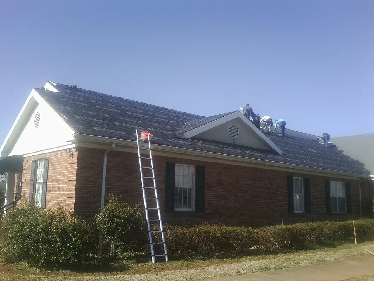 Crew tearing shingles off a brick ranch roof with a ladder set — Emergency Roof Repair work by our crew in Wamego
