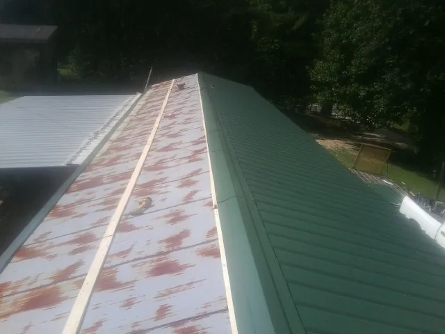 Old rusted panels beside newly installed green metal roofing — Wind Damage Roof Repair by Roofing Brothers in Wamego