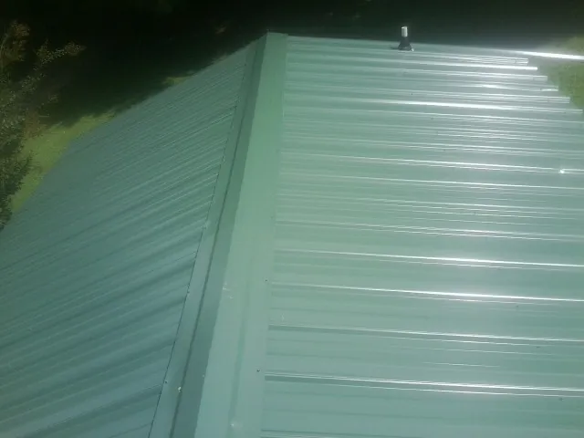 New green metal panels meeting at the ridge of a roof — Flat Roof Repair work by our crew in Wamego