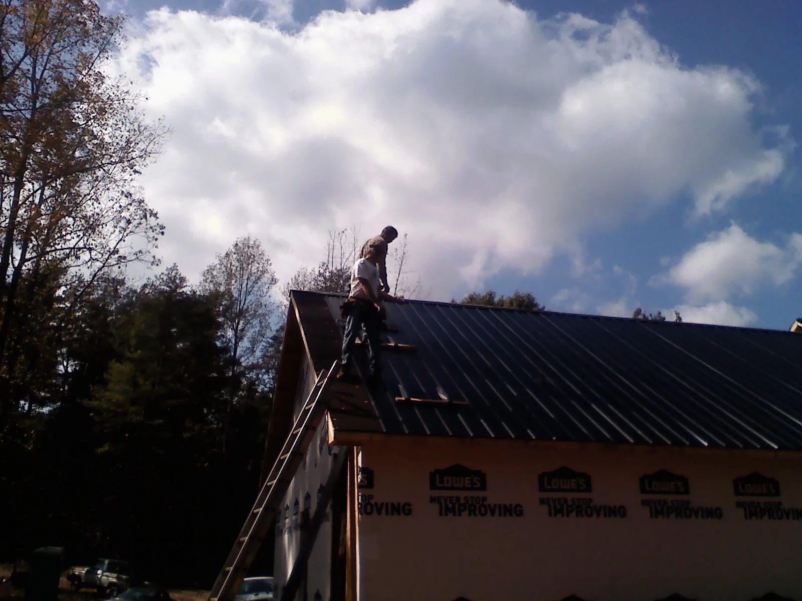 Roofer fastening dark metal panels high against a cloudy sky, from a Roof Inspection job in Wamego