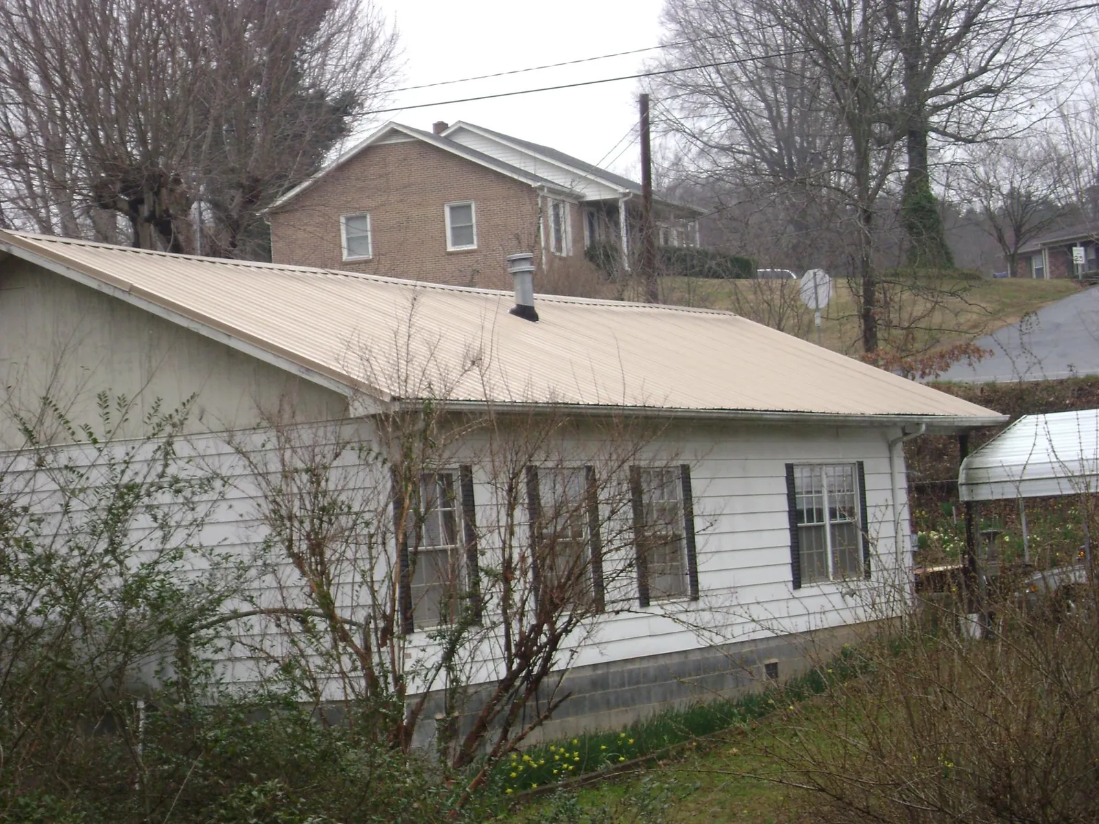 Tan metal roof on a white sided house set into a hillside — Commercial Roofing by Roofing Brothers in Wamego